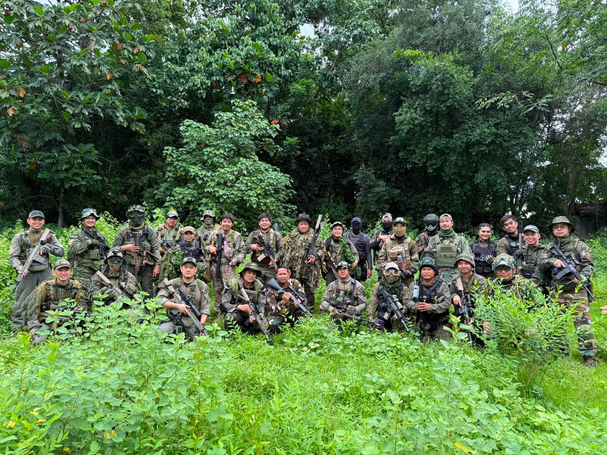 The team assembled in a lush green field with heavy vegetation behind them